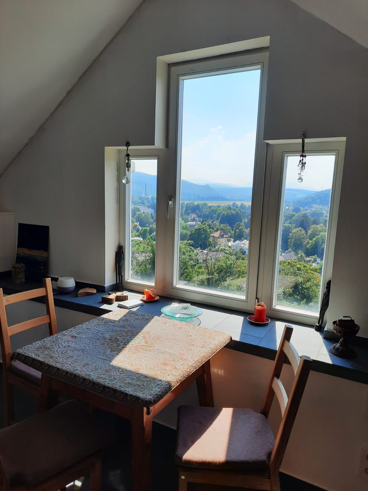 Ein gemütlicher Essbereich mit einem kleinen Tisch und zwei Stühlen vor einem großen Fenster mit Blick auf eine grüne Landschaft.