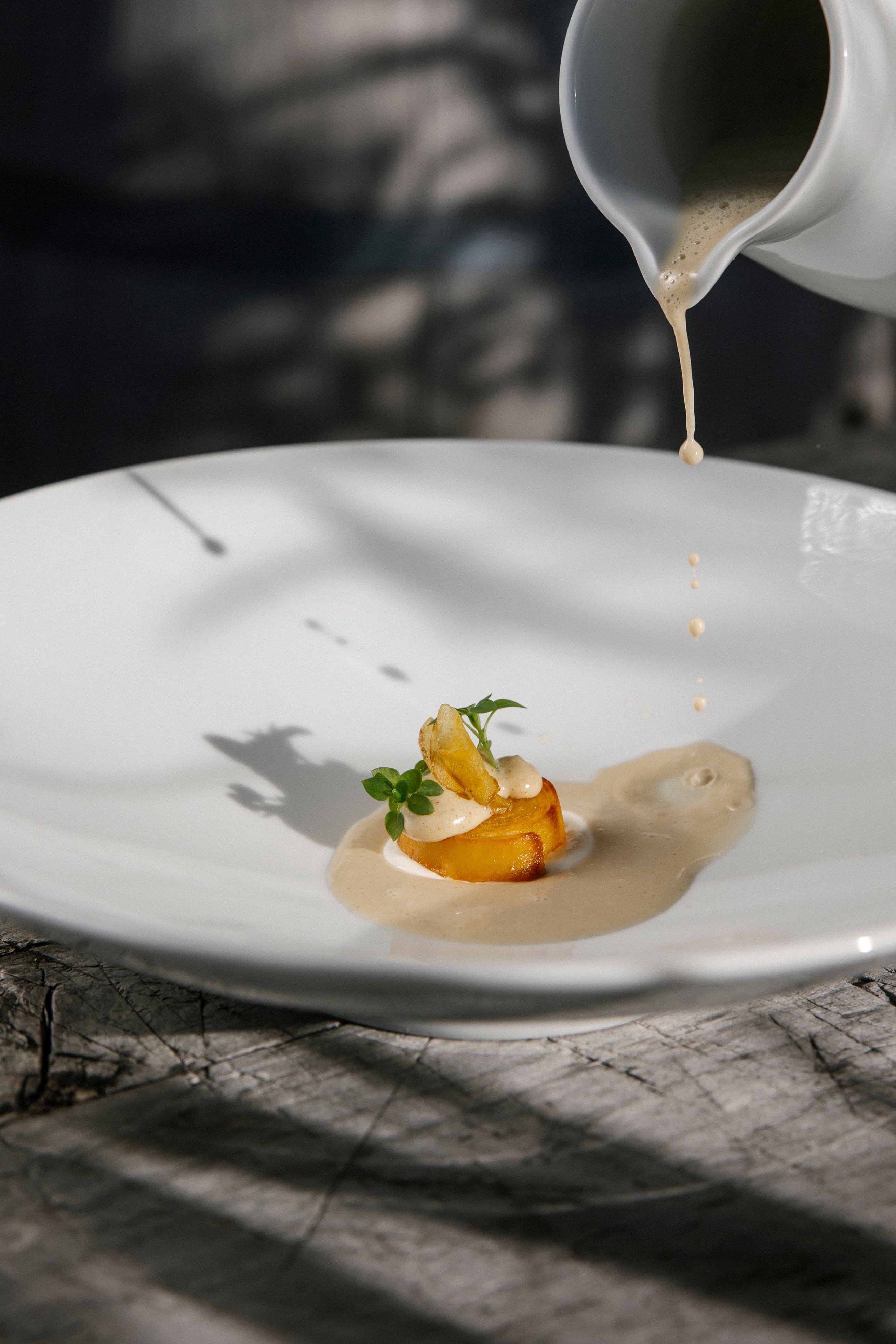 Ein weißes Teller mit einem Gourmetgericht und Soße, die mit einer Kanne auf das Teller gegosen wird.