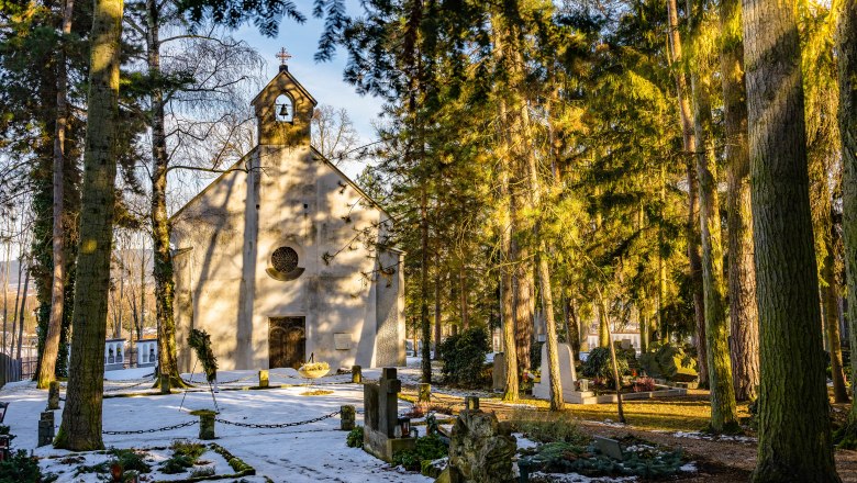 Winterliche Kapelle im Wald mit Gräbern und Schnee.