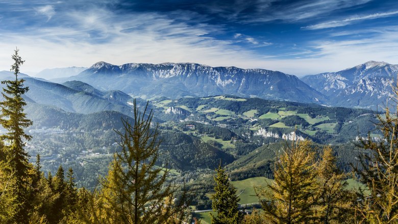 Panoramic view from the Sonnwendstein of wooded hills and mountains under a blue sky.