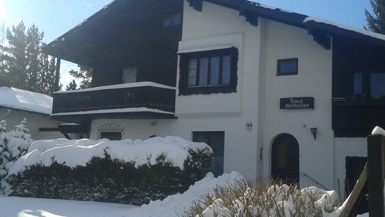 Ein verschneites Haus mit Holzbalkon und Schild 'Haus Almboden'.