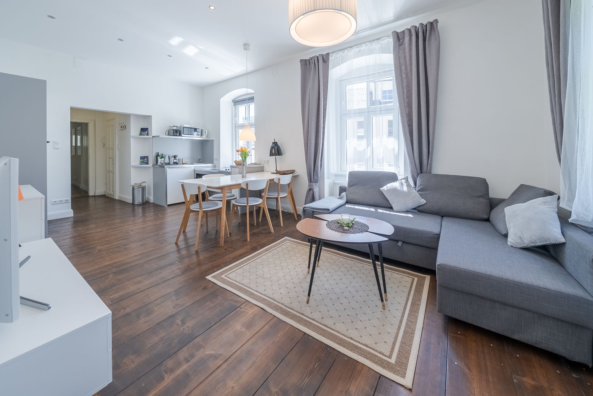 Modern eingerichtetes Wohnzimmer mit grauem Sofa, Esstisch und Küchenzeile.