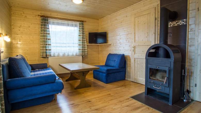 Gem&uuml;tliches Wohnzimmer mit Holzw&auml;nden, blauen Sofas, Holztisch und Kaminofen.