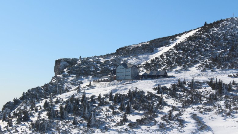 Winterlandschaft mit dem Ottohaus auf einem verschneiten Berg unter klarem Himmel.