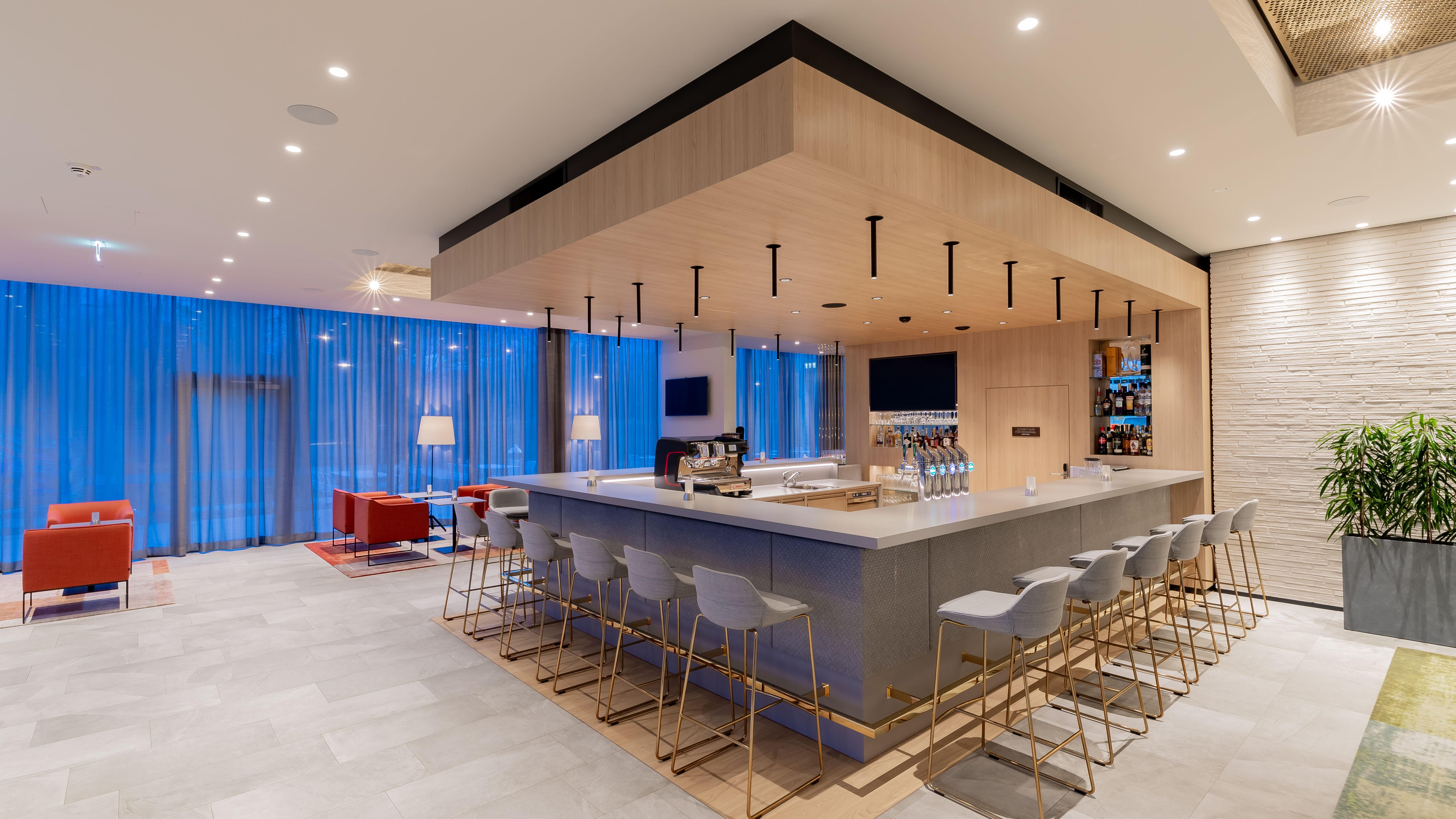 Einladende Bar zwischen Lobby und Restaurant. Graue Hochstühle und Sitzgruppen zum Konsumieren der Speisen und Getränke.