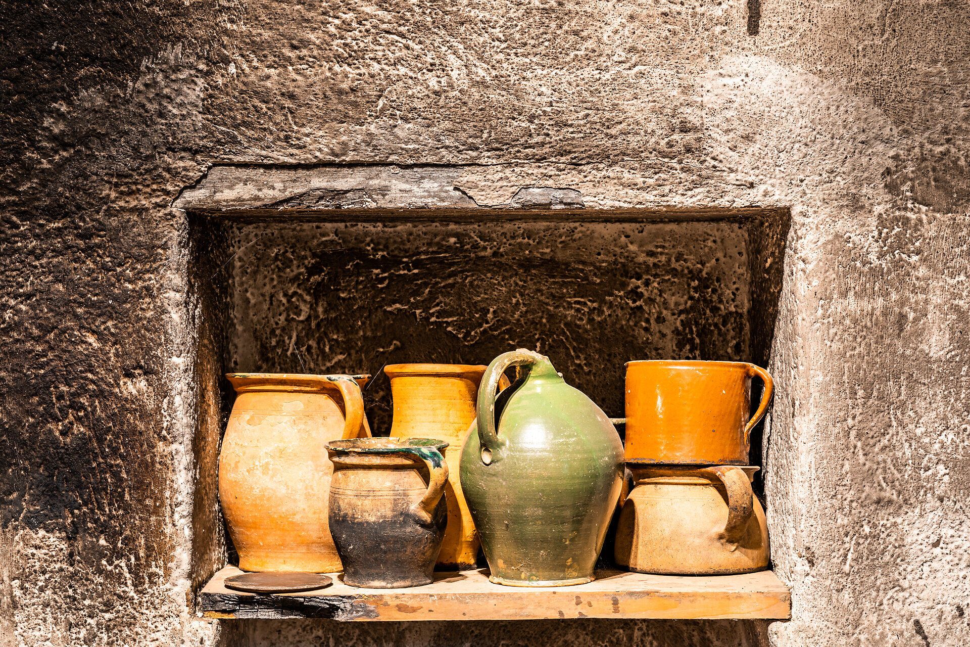 Alte Tongefäße stehen in einem Holzregal in der Wand.