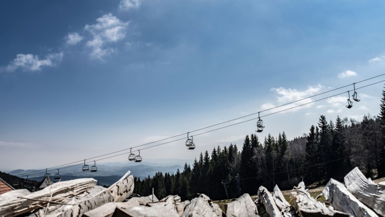View of a cable car above a forest with a blue sky in the background.