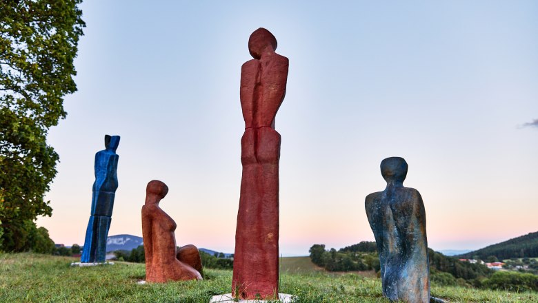 Four colorful sculptures on a meadow at sunset.
