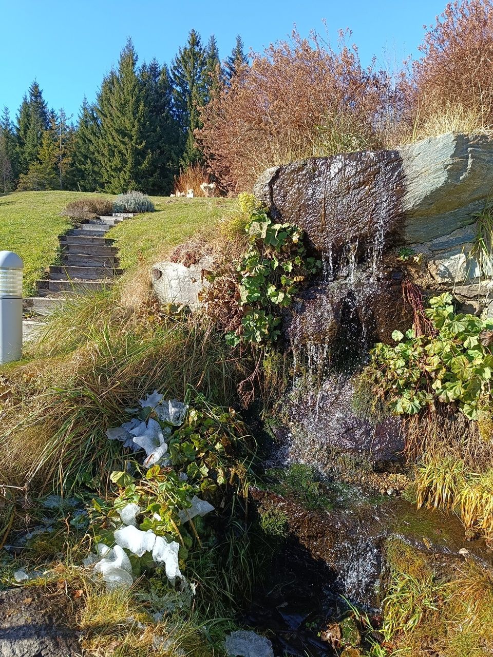 Kleiner Wasserfall in herbstlicher Landschaft mit Bäumen und blauem Himmel.