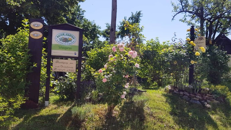 Eingang zu einem Schaugarten mit Schildern und blühenden Rosen.