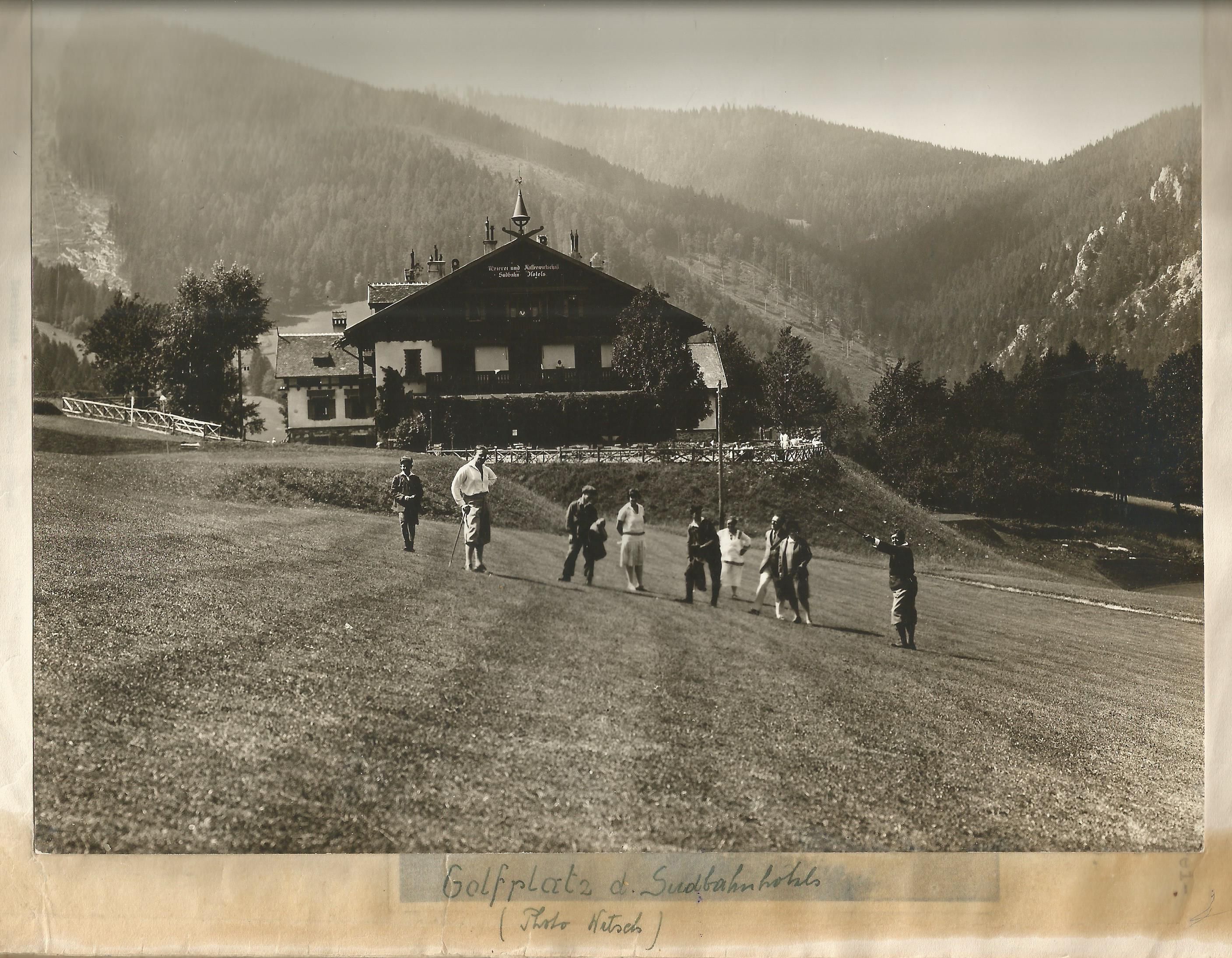 Golfspieler sind auf einem Golfplatz versammelt und ein Gebäude und Berge im Hintergrund
