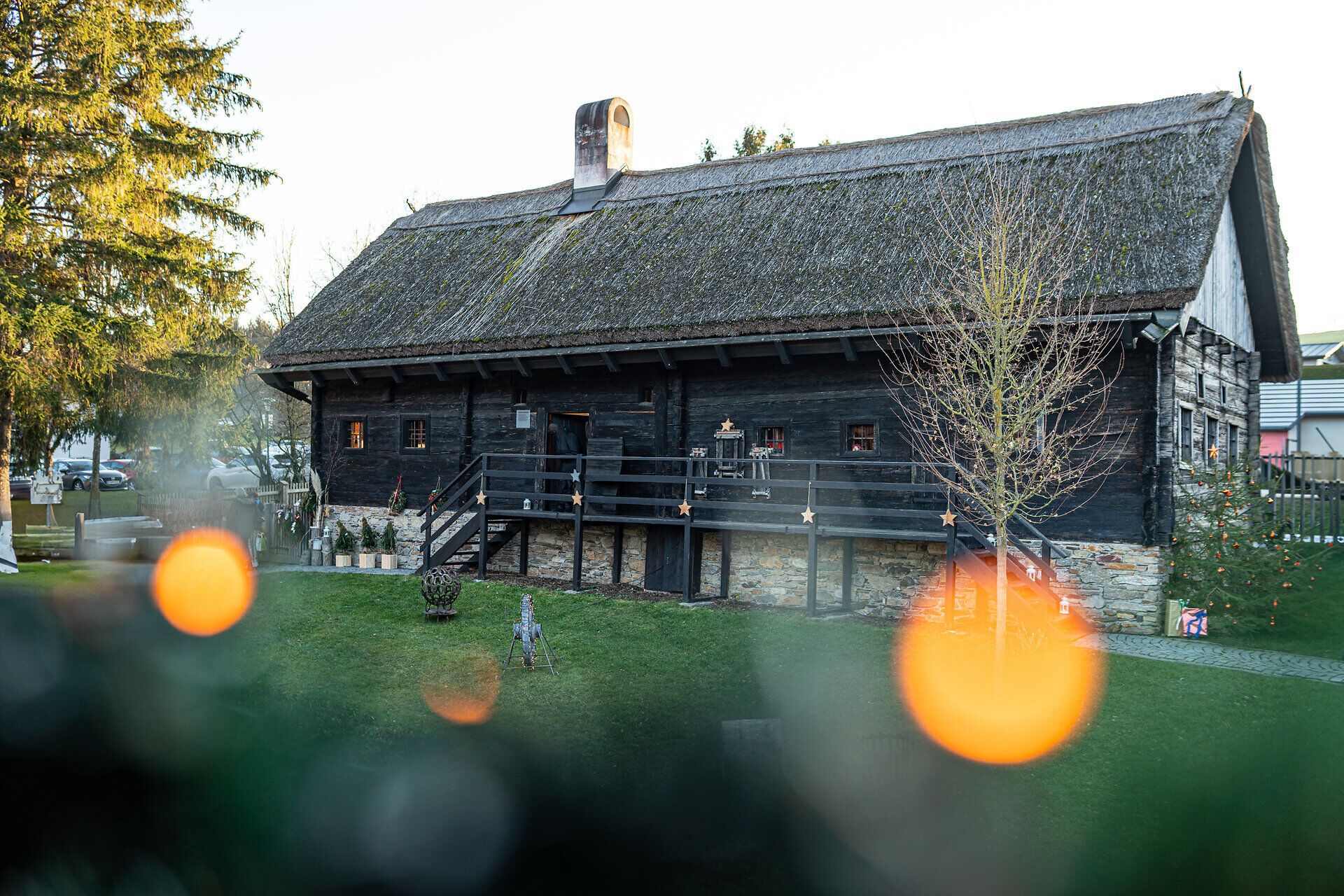 Traditionelles Holzhaus in ländlicher Umgebung, im Vordergrund warme Lichtpunkte.