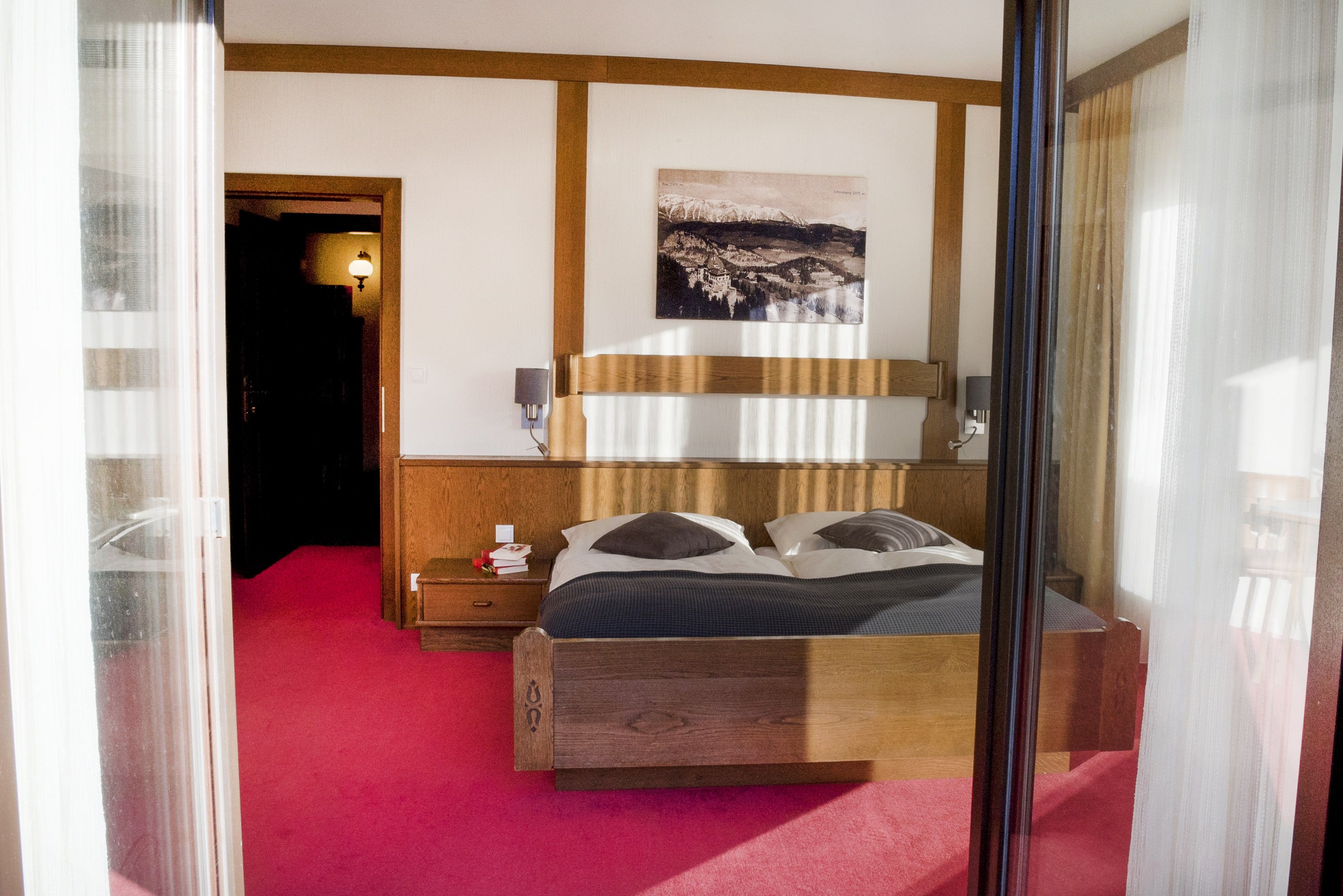 Ein gemütliches Schlafzimmer mit einem Doppelbett, Holzmöbeln und einem Bild an der Wand. Der Boden ist mit einem roten Teppich ausgelegt.