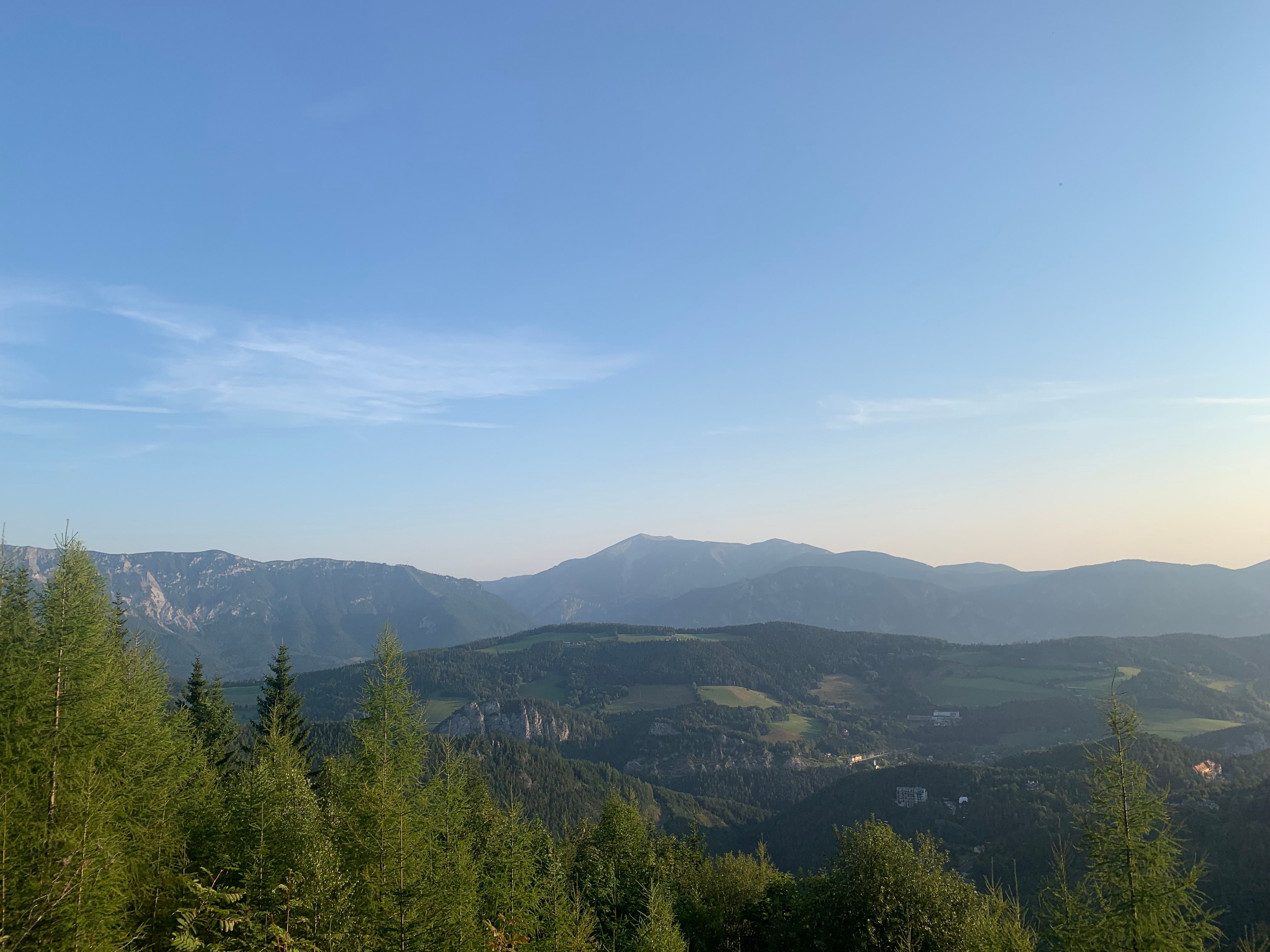Ausblick vom Pinkenkogel auf eine hügelige Landschaft mit Blick auf Semmeringbahn, Rax und Schneeberg