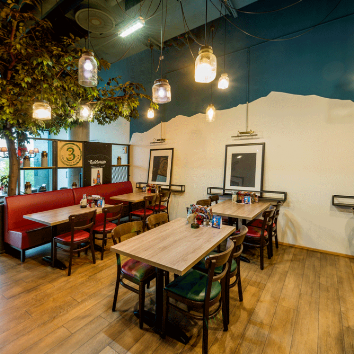 Innenansicht eines Restaurants mit Holztischen, roten Sitzbänken und hängenden Glühbirnen.