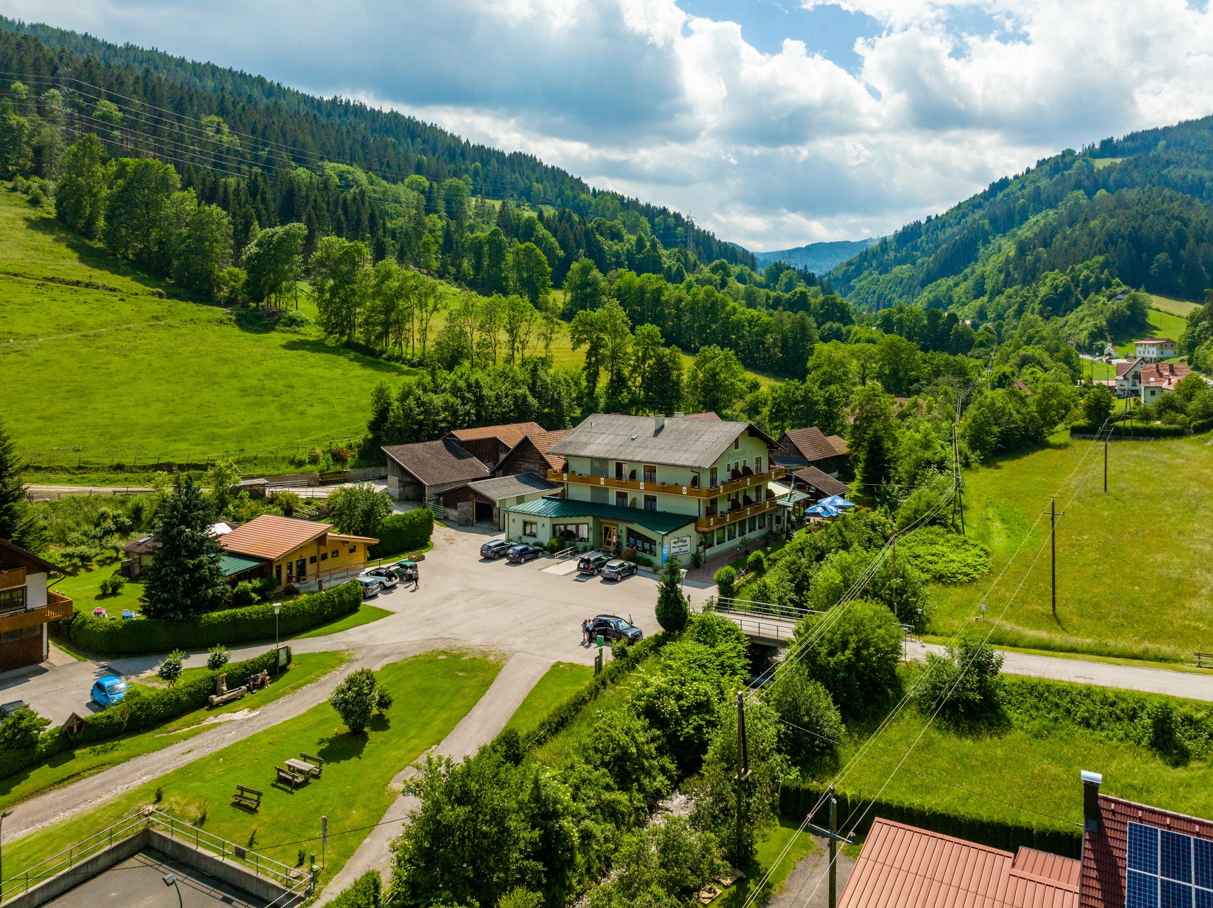 Ländliche Landschaft mit einem großen Gebäude, umgeben von grünen Hügeln und Bäumen.