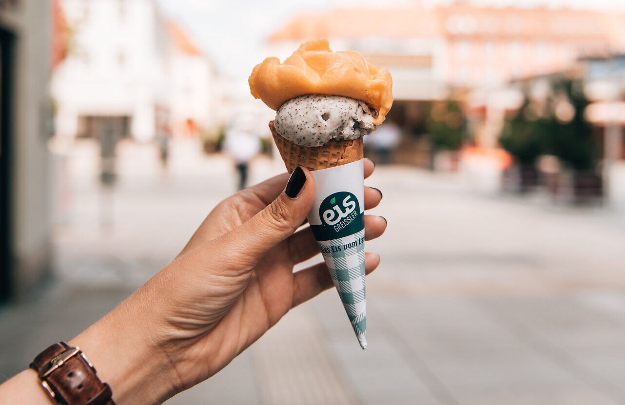 An einem sonnigen Sommertag wird die Freude am Leben durch eine köstliche Eiskreation in einem handlichen Waffelbecher perfekt. Die sanften Farben des Eises harmonieren mit dem strahlend blauen Himmel und laden dazu ein, die warmen Tage in vollen Zügen zu genießen. Ein idealer Moment, um die entspannte Atmosphäre der Stadt zu erleben.