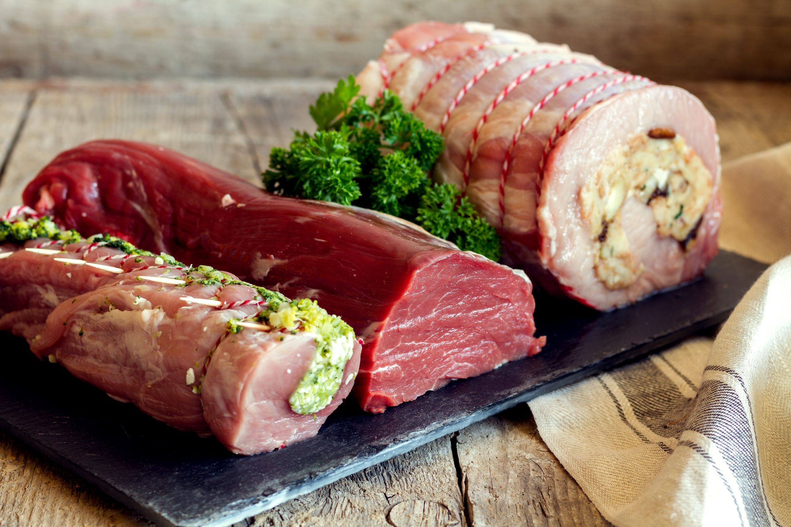 Verschiedene Fleischstücke auf einem Holzbrett, dekoriert mit Kräutern.