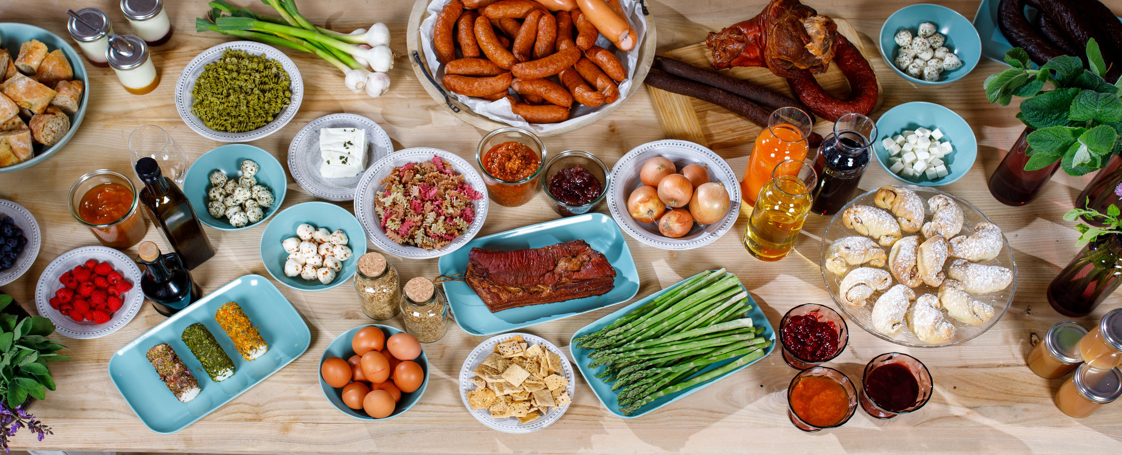 Diverse frische Lebensmittel und Getränke in Tellern, Schüsseln und Krügen auf einem Holztisch.