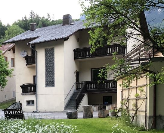 Ein zweistöckiges Haus mit Balkon und Treppe, umgeben von einem grünen Garten mit Blumen.