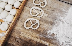 Teiglinge und Brezeln auf einem bemehlten Holztisch.