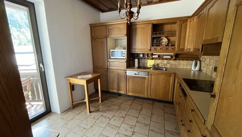 Kitchen with wooden furniture and tiled floor, view of balcony with chairs.