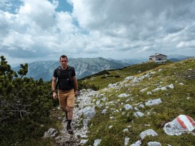 Ein Wanderer genie&szlig;t die frische Bergluft und die atemberaubende Aussicht auf die umliegenden Gipfel. Die sanften H&uuml;gel und das gr&uuml;ne Gras laden dazu ein, die Natur in vollen Z&uuml;gen zu erleben. Hier, in den Wiener Alpen, wird jeder Schritt zu einem unvergesslichen Abenteuer.