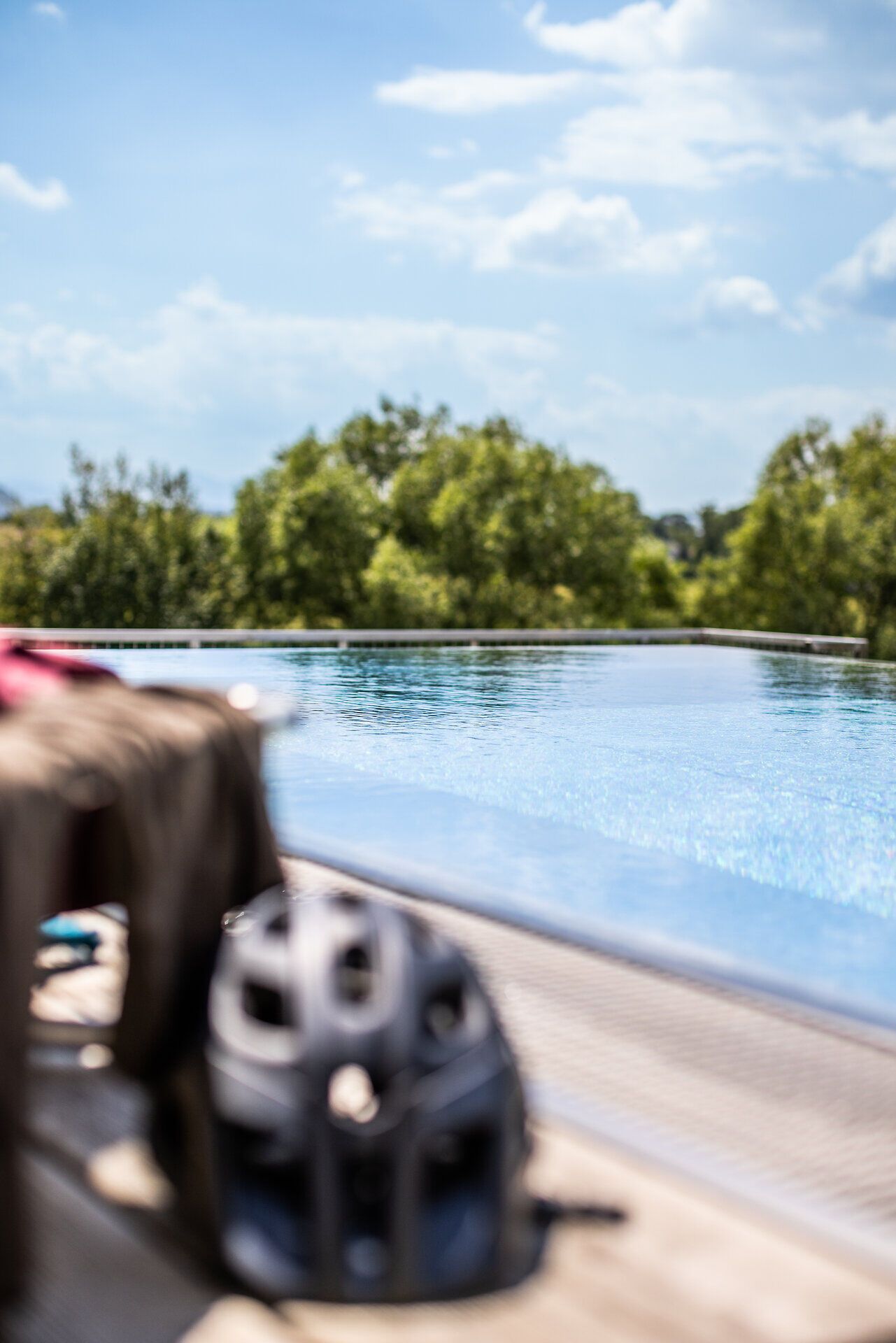 Auf einem Liegestuhl liegen Radkleidung und Radhelm vor dem Infinity Pool des Grandhotel Niederösterreichischer Hof mit Blick ins Grüne.