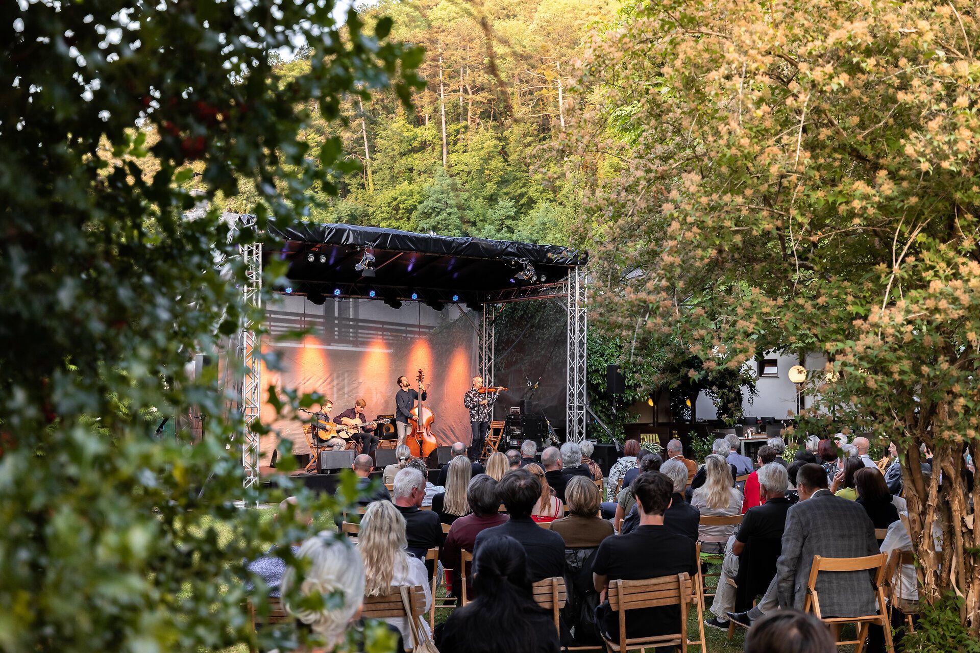Auf einer Bühne geben vier Musiker ein Open Air Konzert vor Publikum.