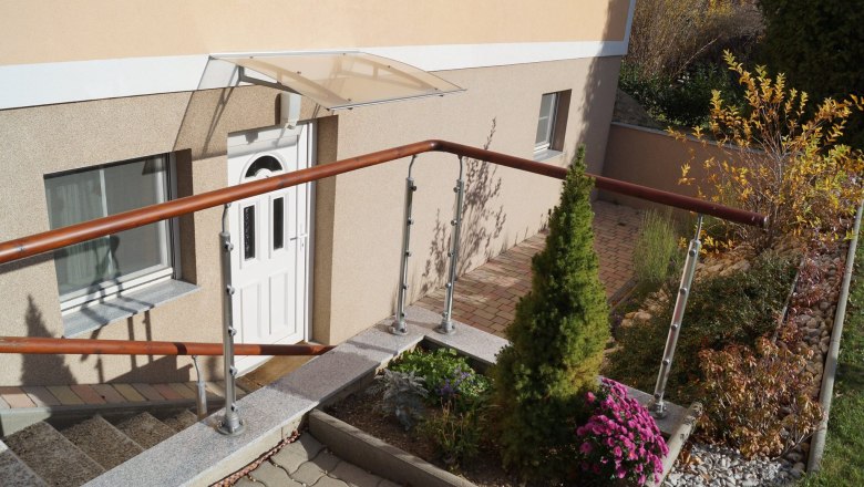 Eingangsbereich eines Hauses mit weißer Tür, Geländer und Garten.