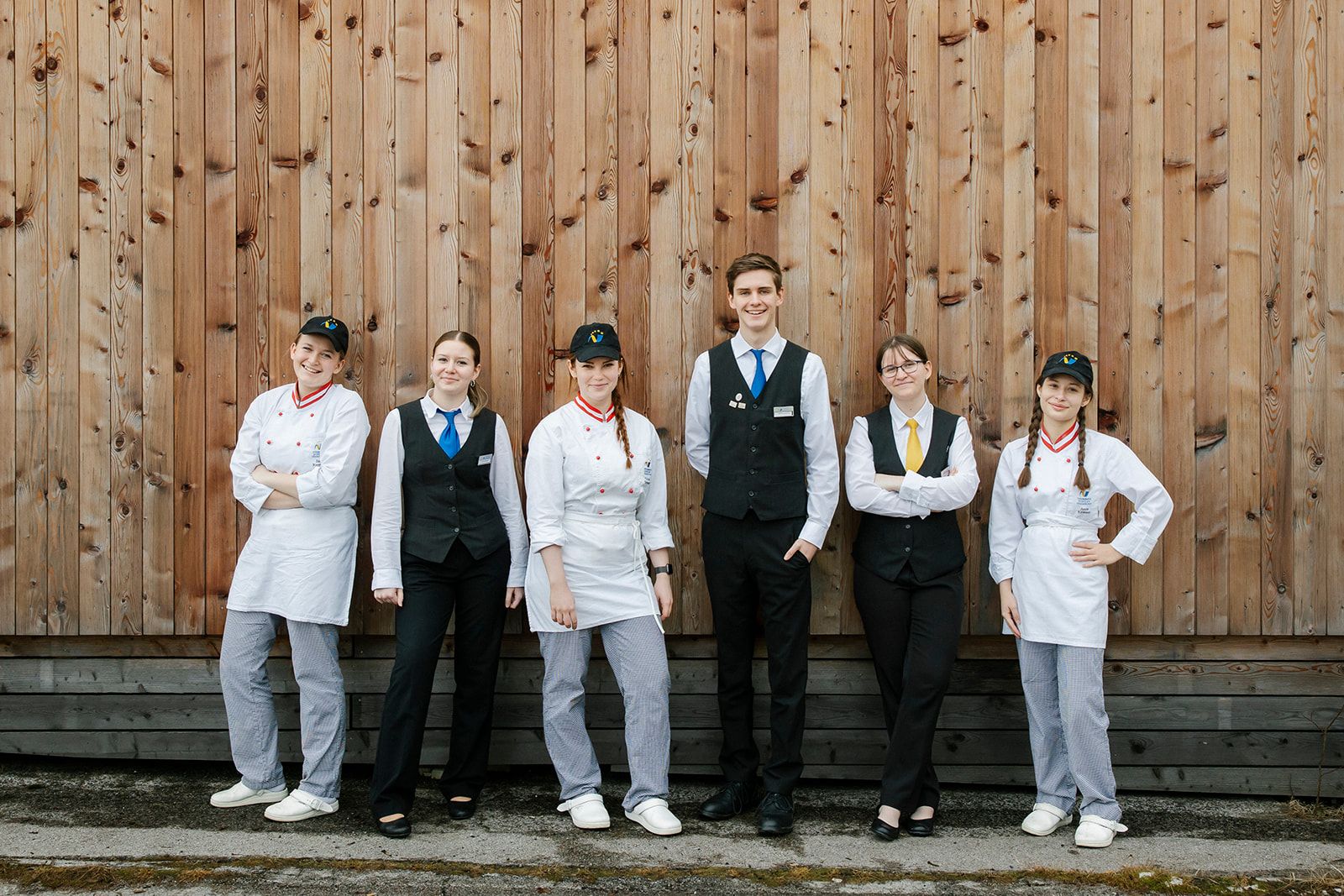 Sechs junge Menschen in Uniformen vor einer Holzwand.