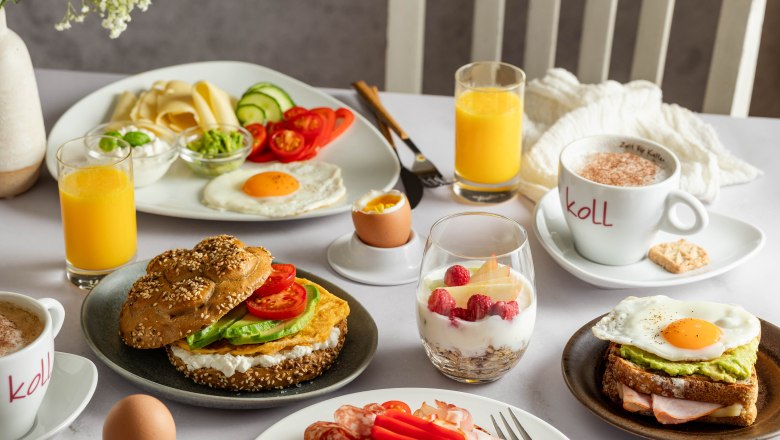 Frühstückstisch mit Brötchen, Aufschnitt, Spiegelei, Joghurt mit Beeren, Orangensaft und Kaffee.