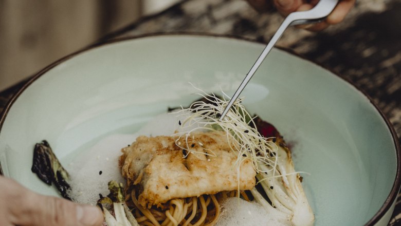 Egy tányér sült hal tésztán, csírával és zöldségekkel díszítve.