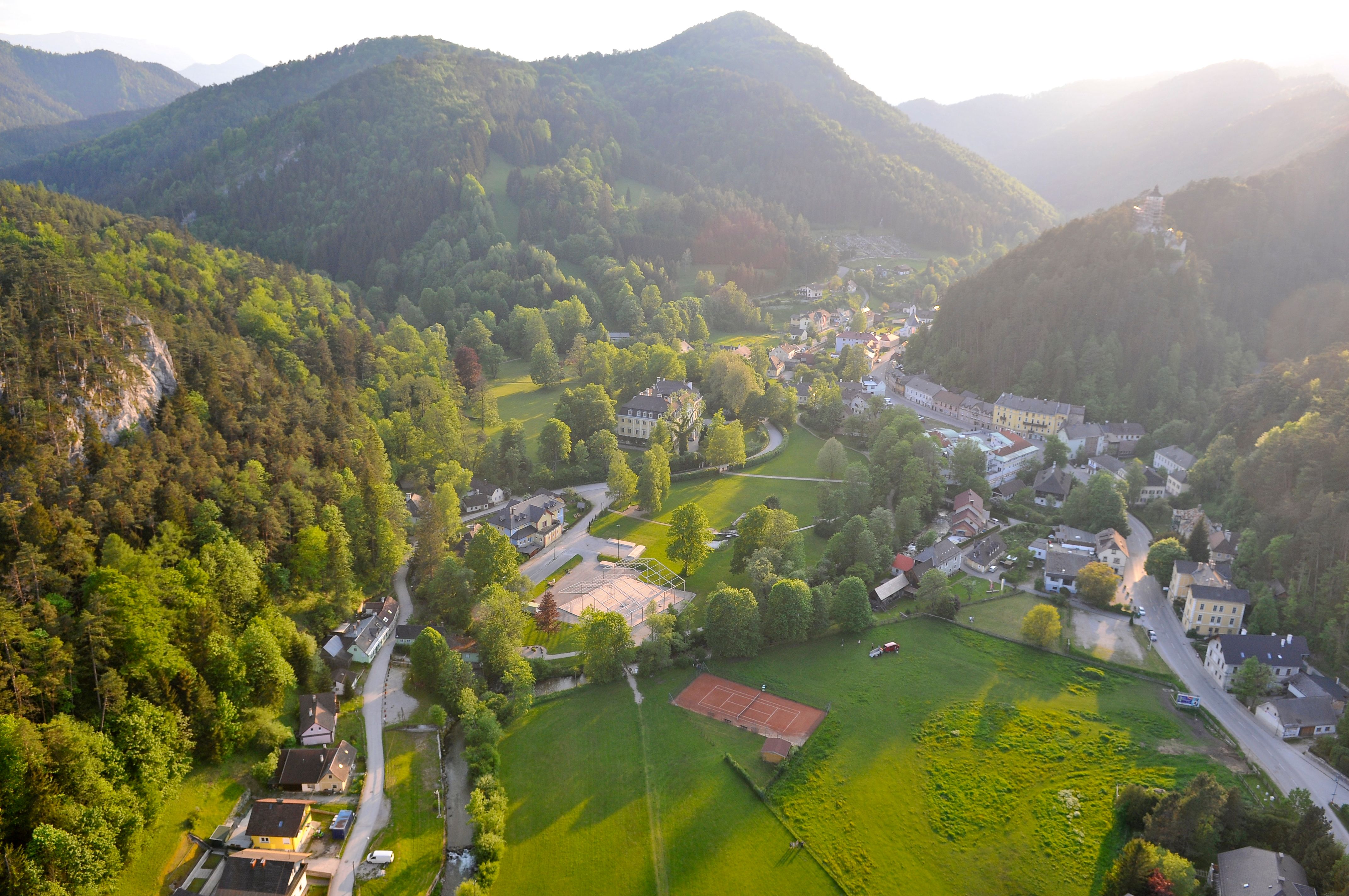 Luftaufnahme von Gutenstein, umgeben von grünen Hügeln und Wäldern, mit Gebäuden und Straßen im Tal.