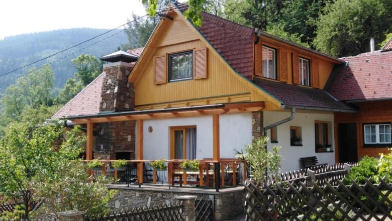 Ein traditionelles Ferienhaus mit Holzveranda und Schindeldach, umgeben von Bäumen und Bergen.