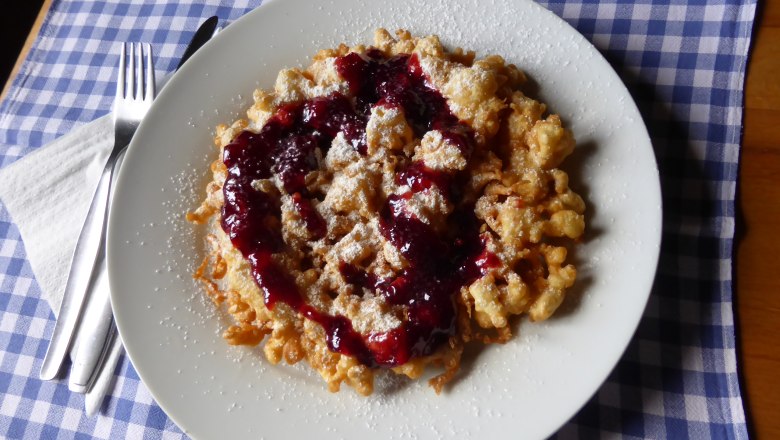 Ein Teller mit Kaiserschmarrn und roter Grütze auf einem blau-weiß karierten Tuch.