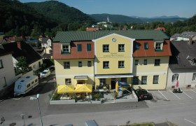 Gelbes Gebäude mit der Aufschrift 'Gasthof Zur Alten Schule', umgeben von Hügeln und Bäumen.