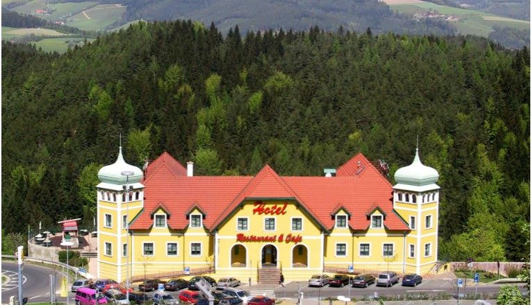 Yellow hotel with red roofs in a green, hilly landscape.