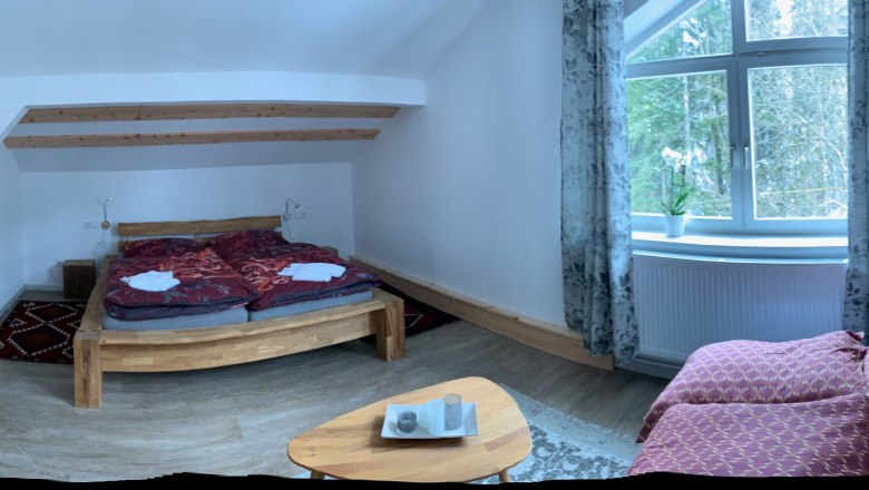 Gem&uuml;tliches Schlafzimmer mit Holzbett, Sofa und gro&szlig;em Fenster mit Vorh&auml;ngen.