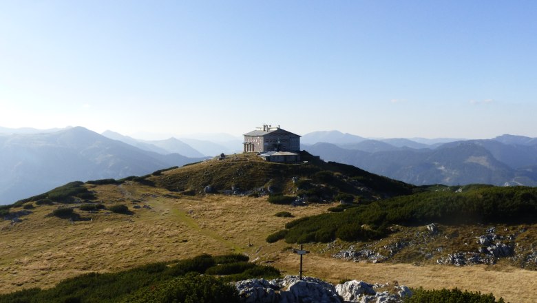 Mountain hut on a hill with a mountain panorama in the background.
