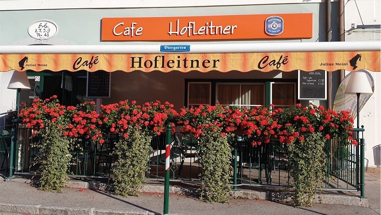Au&szlig;enansicht des Caf&eacute; Hofleitner mit roten Blumen und Markise.