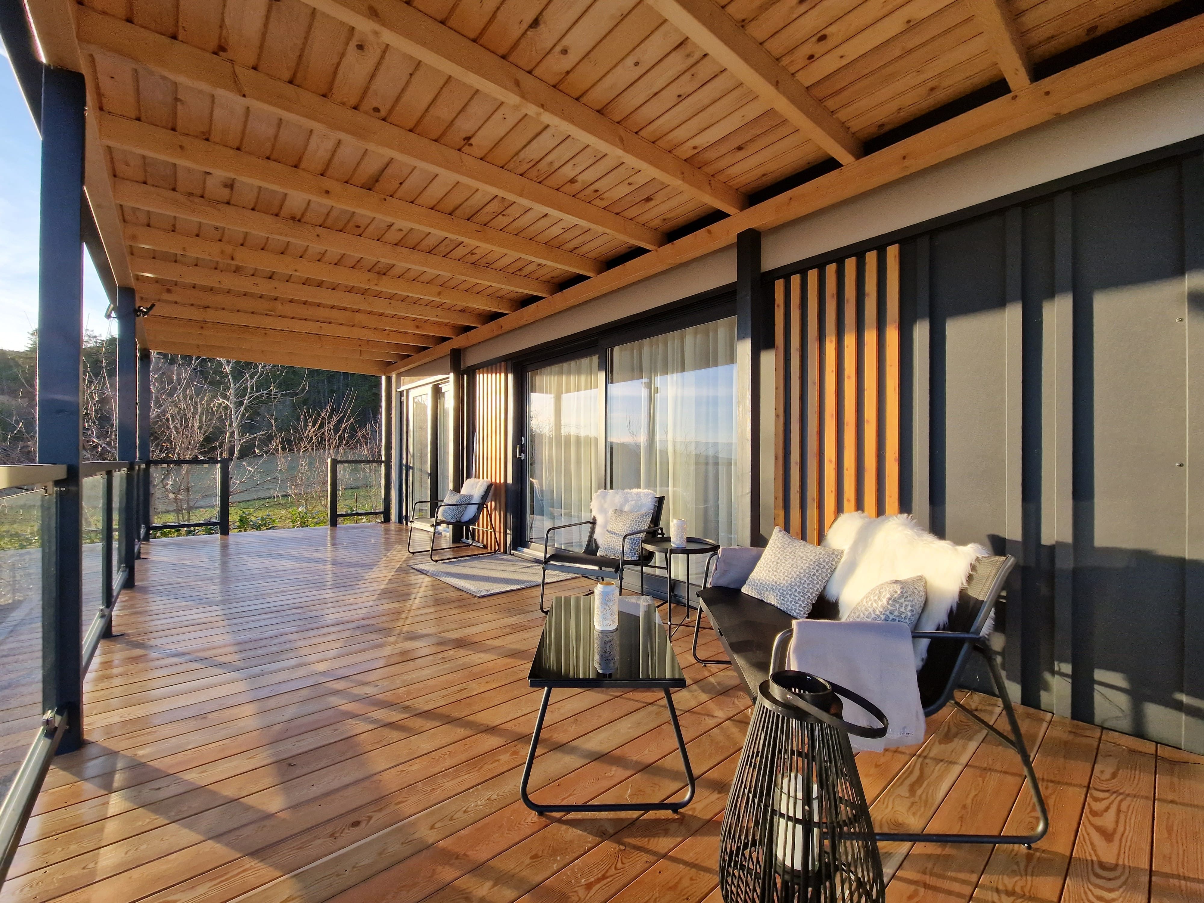 Moderne Terrasse mit Holzboden, Glasgeländer und gemütlichen Sitzmöbeln.