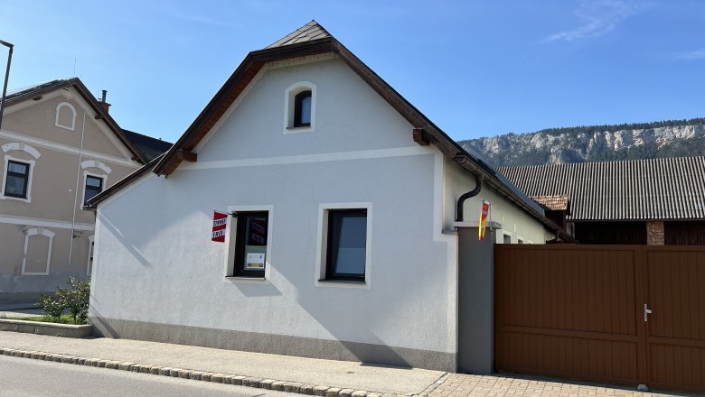 A small, white vacation home with a brown gate and a mountain backdrop.