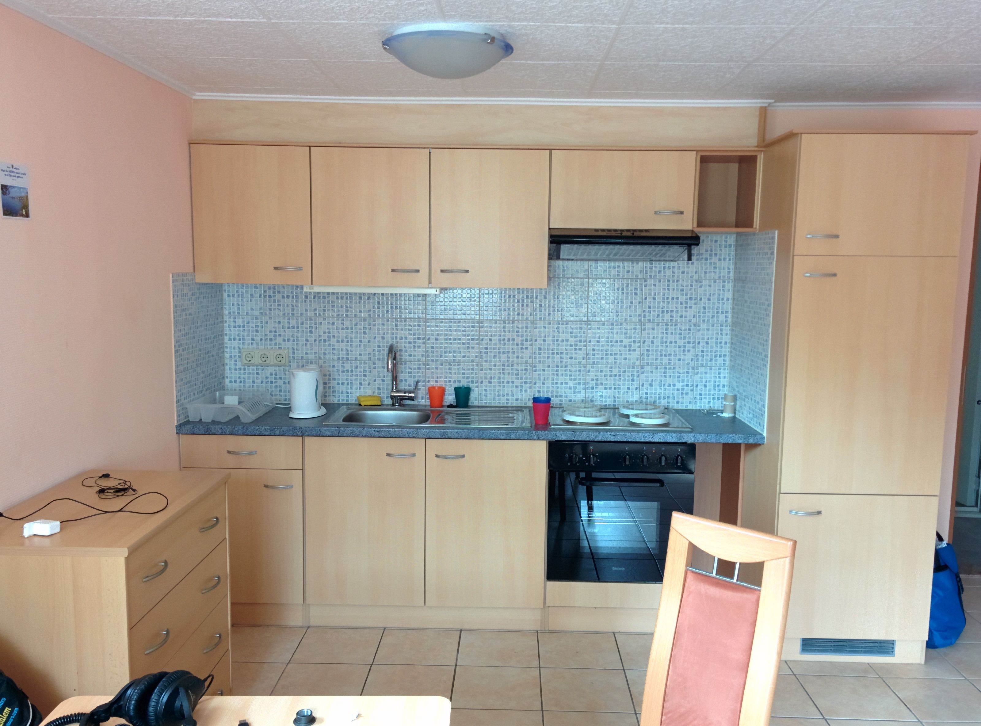 Kleine Küche mit Holzschränken, Spüle, Herd und Fliesenrückwand.