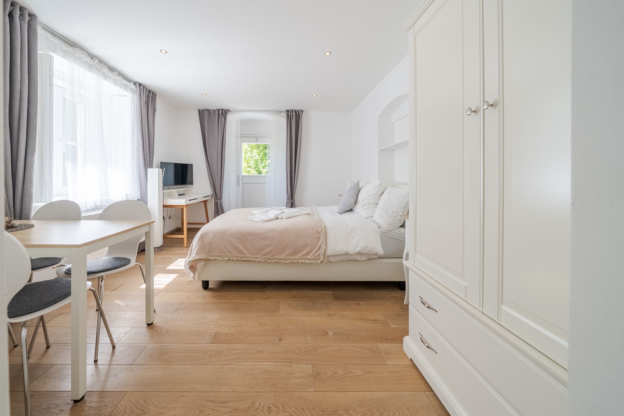 Helles, modern eingerichtetes Zimmer mit Bett, Tisch, Stühlen und Fernseher.