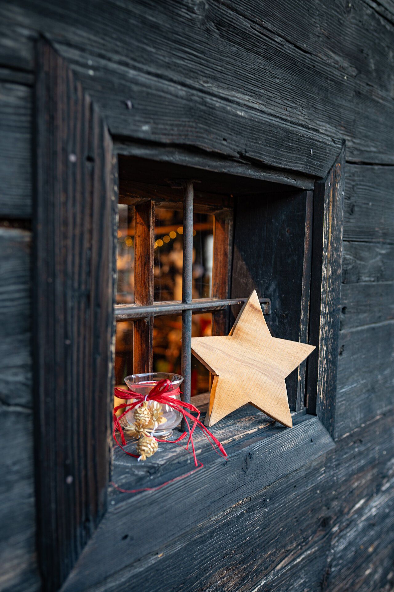 Fenster eines Hauses mit Holzvertäfelung mit leuchtendem Stern und weihnachtlicher Dekoration.