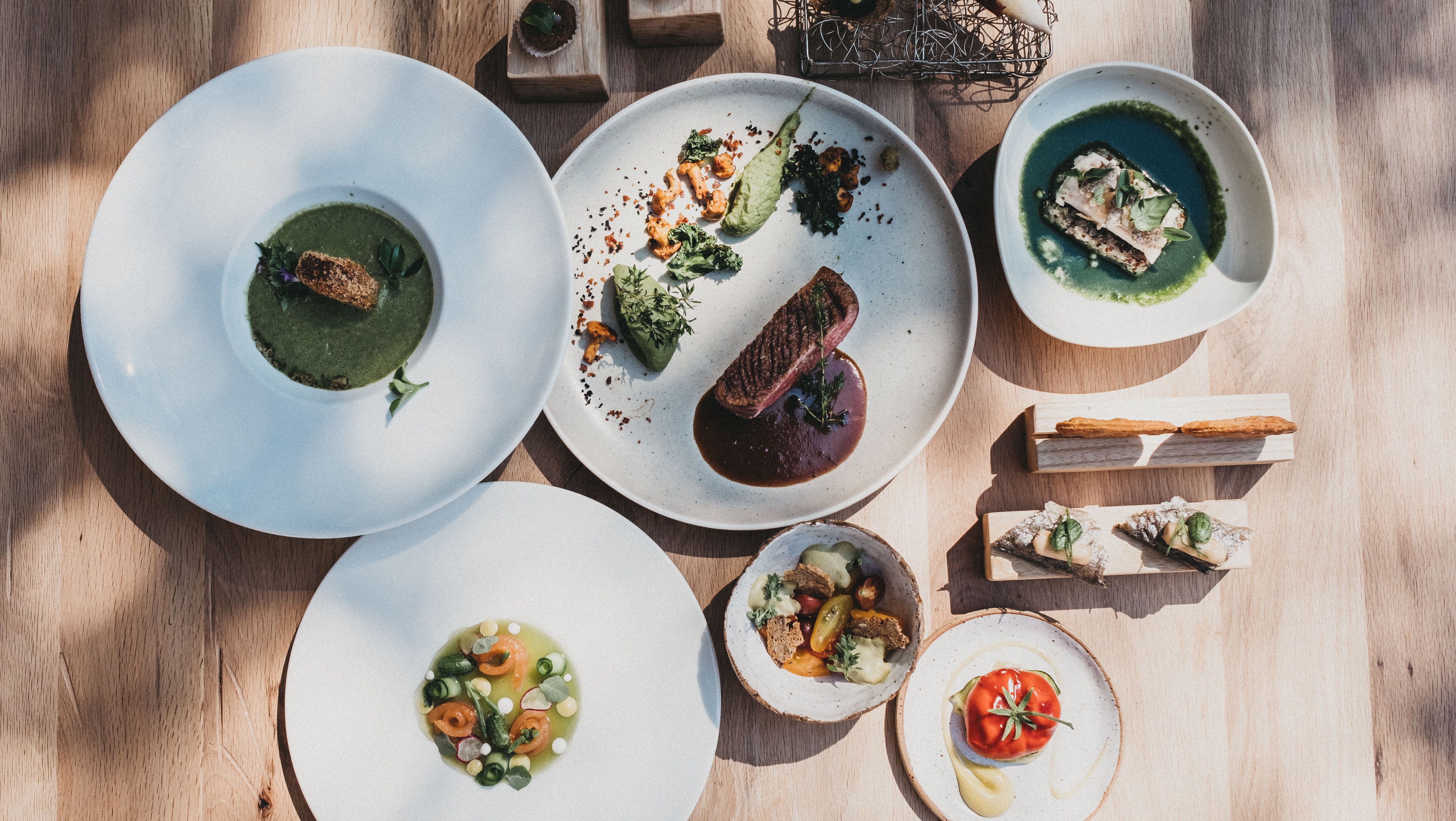 Mehrere Teller mit verschiedenen Gourmetgerichten auf einem Holztisch.