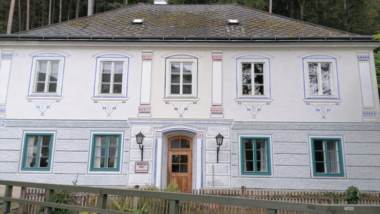Historic building with ornate windows and wooden door, surrounded by forest.