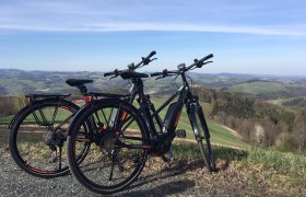Two e-bikes are parked on a hill overlooking a hilly landscape.