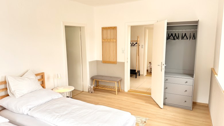 Helles Schlafzimmer mit Bett, Kleiderschrank und Bank.